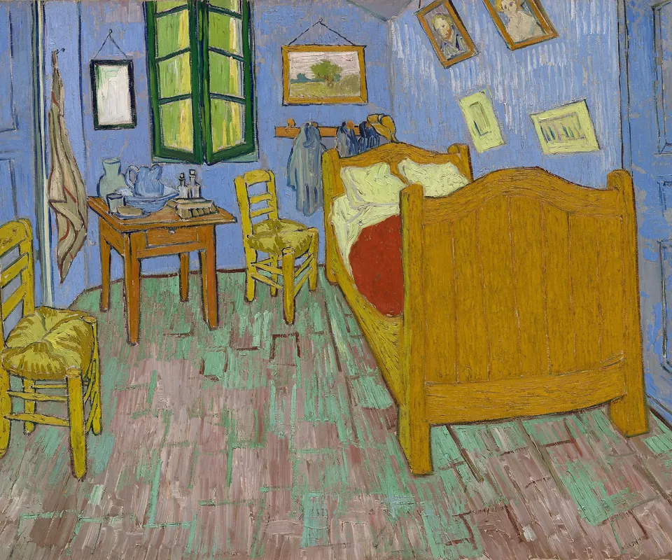 Detail of The Bedroom by Vincent van Gogh. A wooden bed and two chairs stand in a brightly colored bedroom.